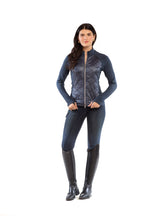 Woman wearing a blue metallic jacket, jeans, and black riding boots on a white background