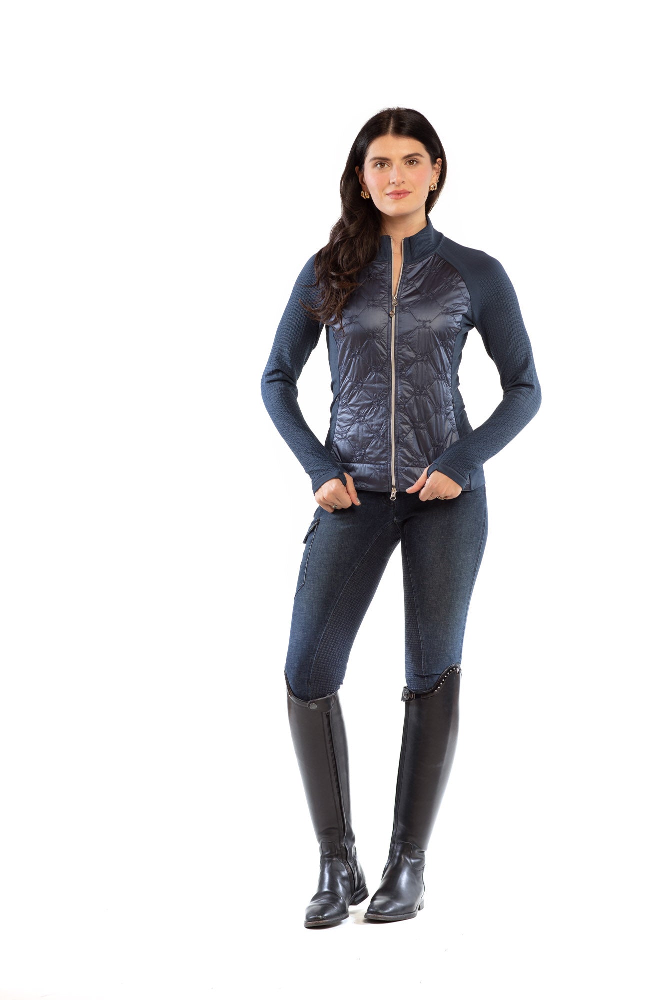 Woman wearing a blue metallic jacket, jeans, and black riding boots on a white background