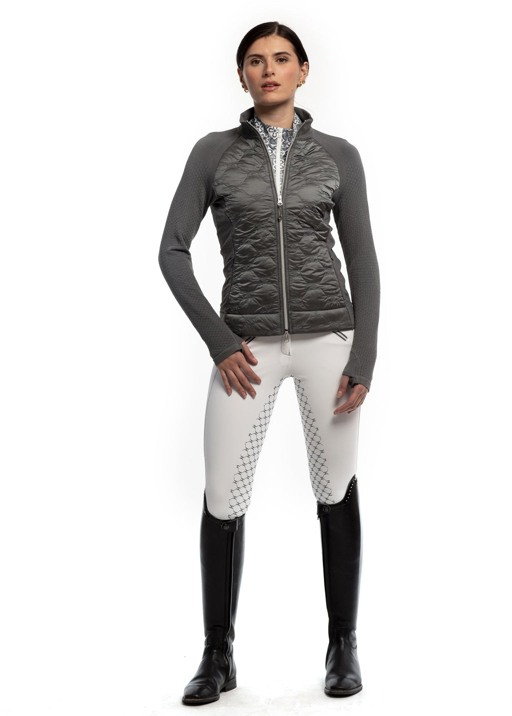 Woman wearing a gray quilted vest, white pants with black pattern, and black riding boots on a white background