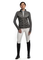 Woman wearing a gray quilted vest, white pants with black pattern, and black riding boots on a white background
