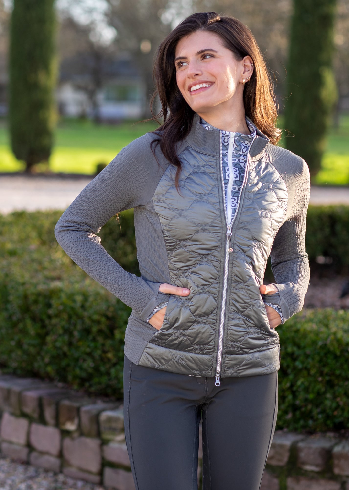 Woman wearing a green quilted jacket outdoors with greenery in the background