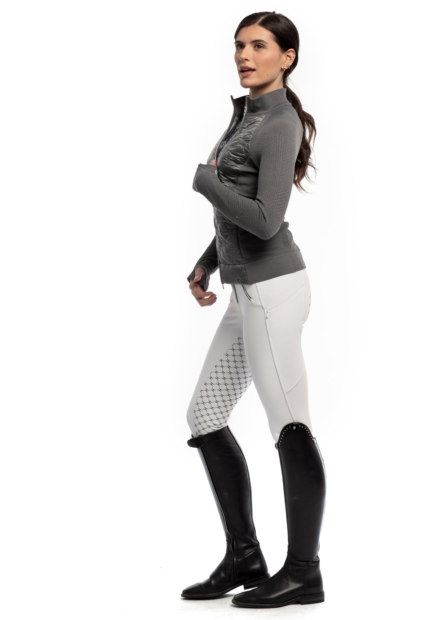 Woman wearing a gray jacket, white pants with black pattern, and black riding boots on a white background