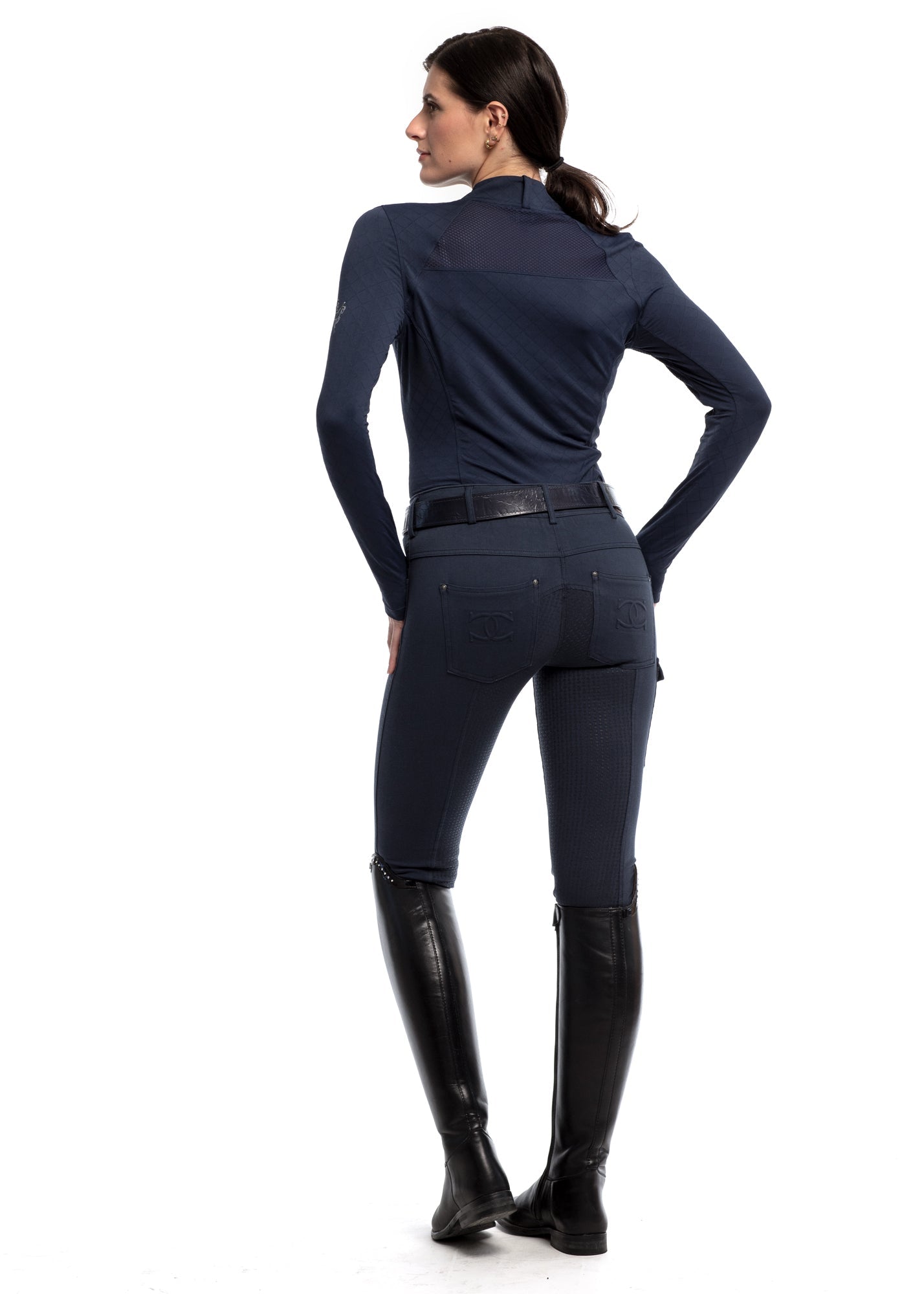 Person wearing a navy riding outfit with black boots on a white background