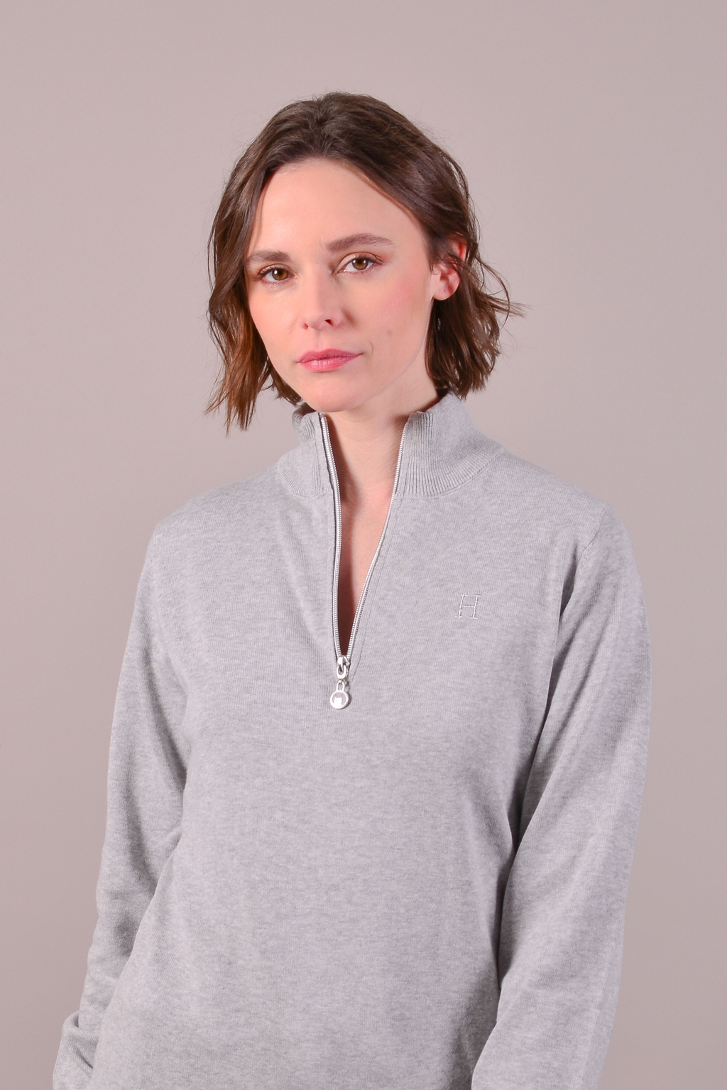 Woman wearing a gray zip-up sweatshirt against a plain background
