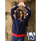 Person wearing a navy and red jacket with a logo, standing against hay bales.