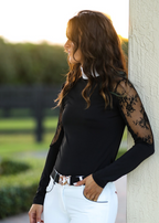 Woman wearing a black long-sleeve top with lace sleeves against a blurred outdoor background