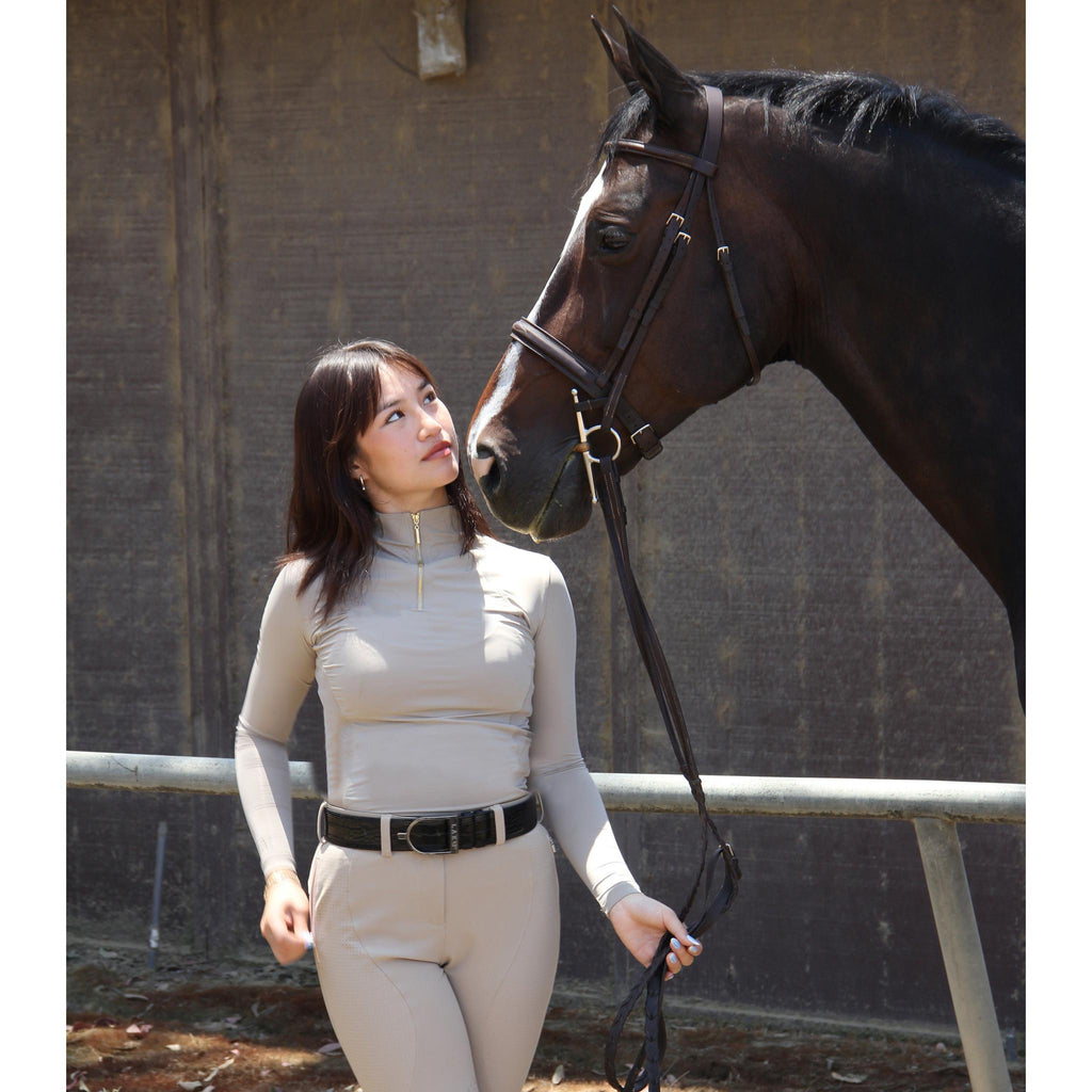 Woman in equestrian attire standing next to a horse in an indoor setting