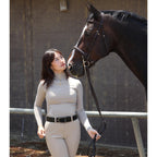 Woman in equestrian attire standing next to a horse in an indoor setting