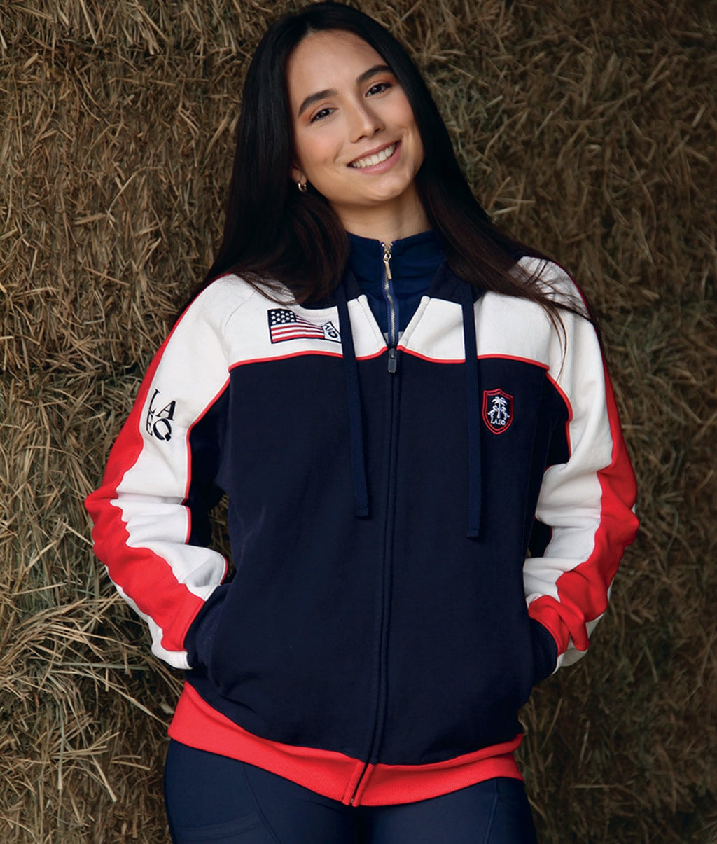 Person wearing a navy, white, and red jacket with an American flag emblem against a hay bale background.