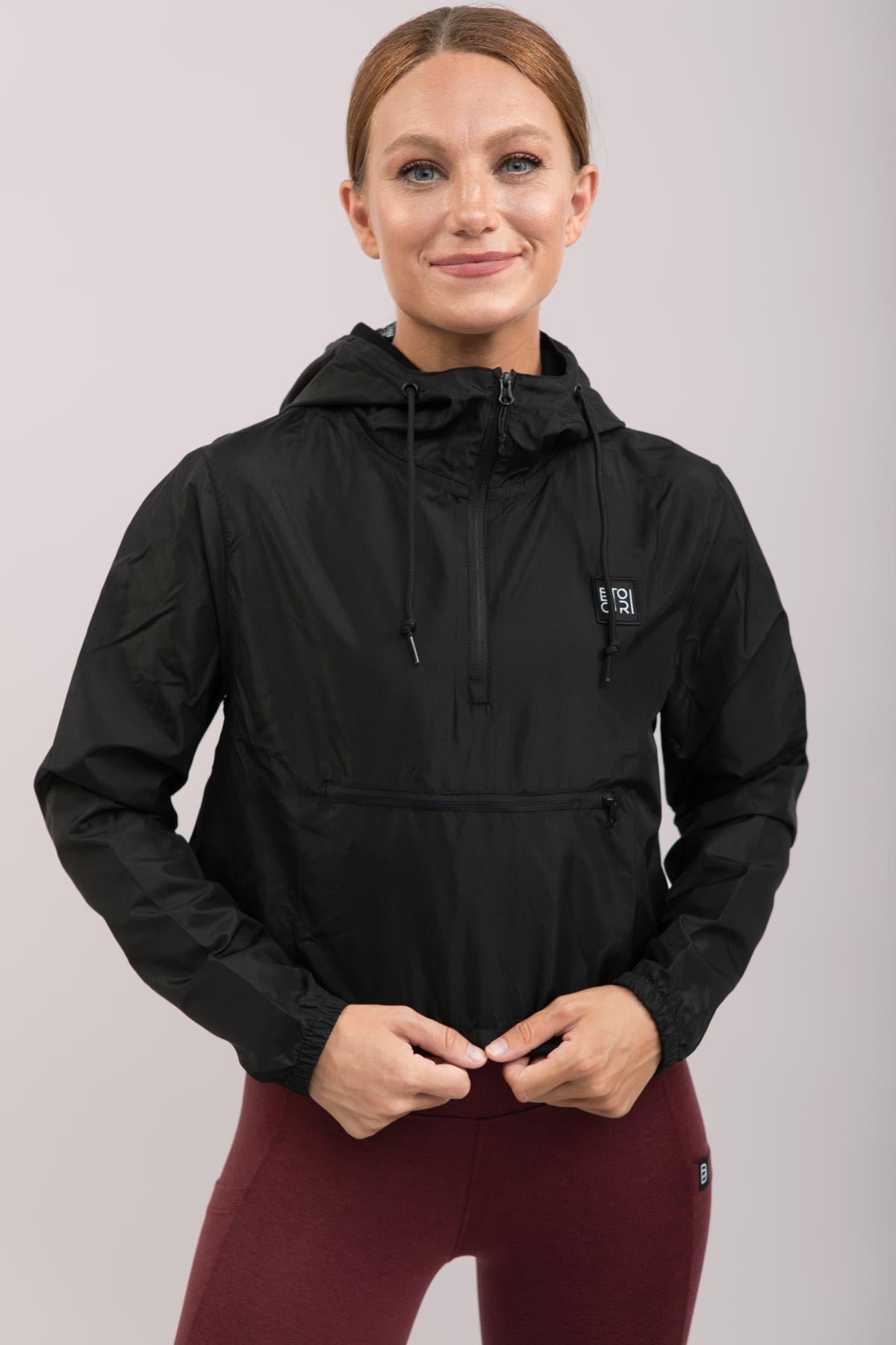 Person wearing a black jacket with a logo on a light gray background