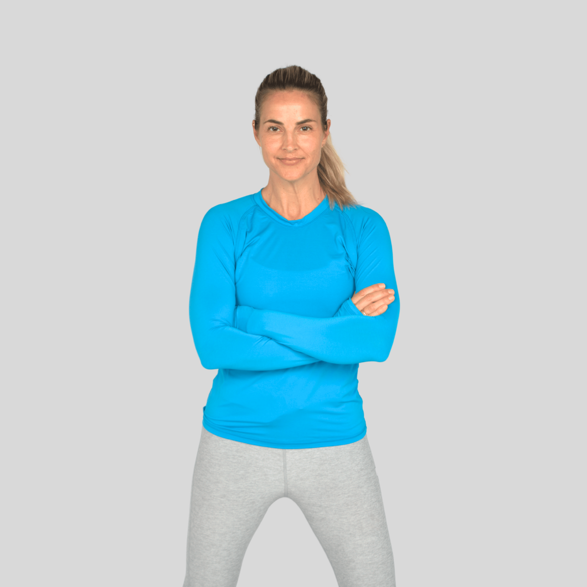 Woman wearing a blue long-sleeve top and gray leggings on a light gray background