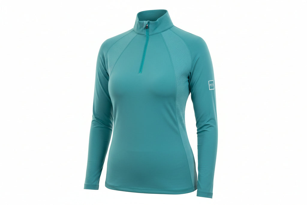 teal long-sleeve top and dark blue jeans outdoors with greenery in the background