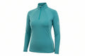 teal long-sleeve top and dark blue jeans outdoors with greenery in the background