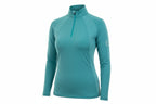 teal long-sleeve top and dark blue jeans outdoors with greenery in the background