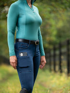 Person wearing a teal long-sleeve top and blue jeans with a blurred natural background