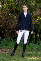 Woman in airbag-compatibe show jacket and equestrian attire standing outdoors with greenery in the background