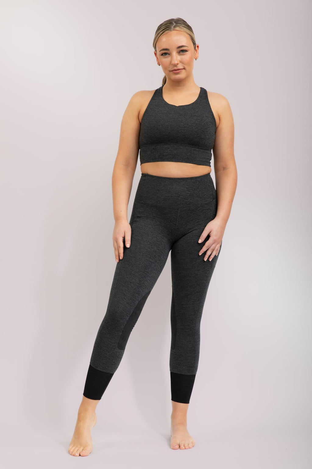 Woman wearing a dark grey equestrian athletic outfit on a gray background