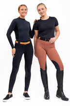 Two women wearing equestrian attire with black and brown pants on a white background