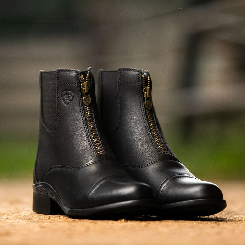 Pair of black leather boots with gold zippers on a blurred natural background