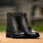 Pair of black leather boots with gold zippers on a blurred natural background