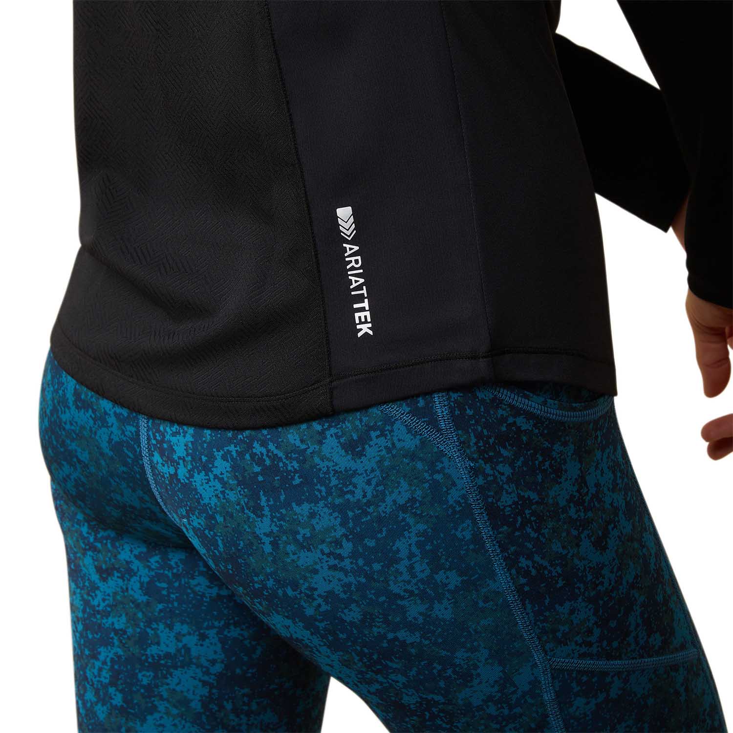 Person wearing a black jacket with AriatTek logo and blue patterned pants on a white background