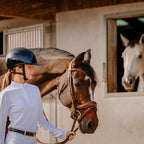 Woman in equestrian attire standing next to a brown horse in a stable.