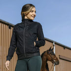 Woman wearing a black jacket with a horse in the background