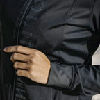 Close-up of a person wearing a black jacket with a brand logo on the chest.