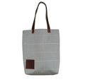 Gray tote bag with brown leather accents on a striped background