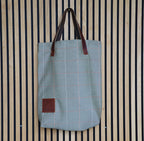 Blue tote bag with brown leather handles and patch on a striped background