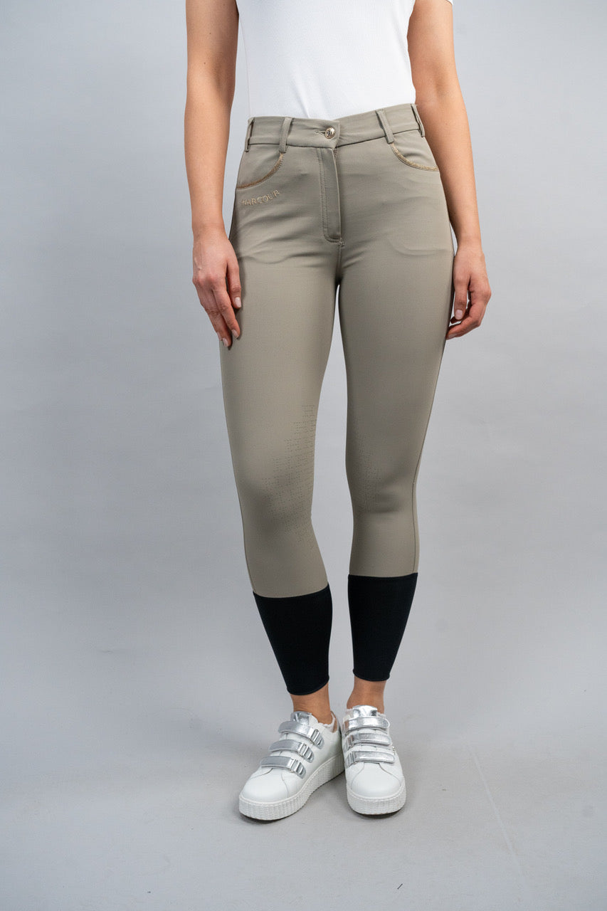 Person wearing beige riding pants with black ankle cuff on a gray background