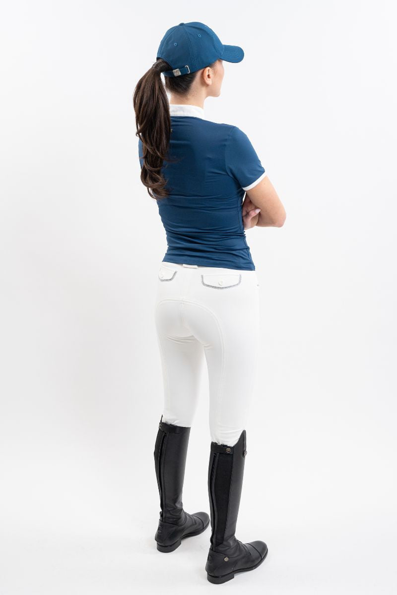 Person wearing a blue cap, blue show jumping shirt, white breeches, and black riding boots on a white background