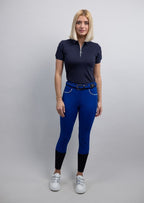 Woman wearing a navy polo shirt and blue breeches on a gray background