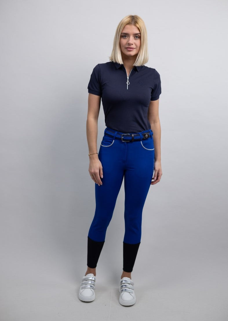 Woman wearing a navy polo shirt and blue breeches on a gray background
