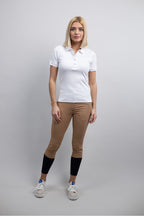 Woman wearing a white polo shirt, brown equestrian riding leggings, and black knee-high socks on a gray background