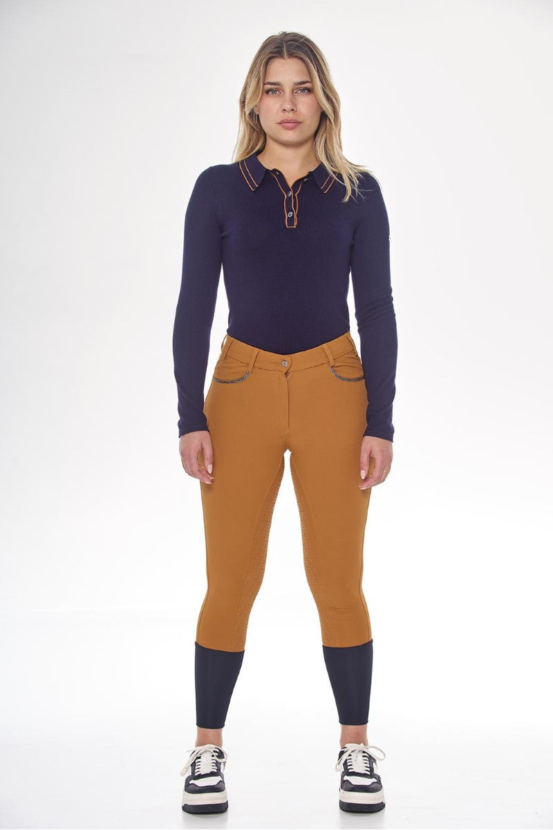 Woman wearing a navy long-sleeve top and mustard riding pants on a white background