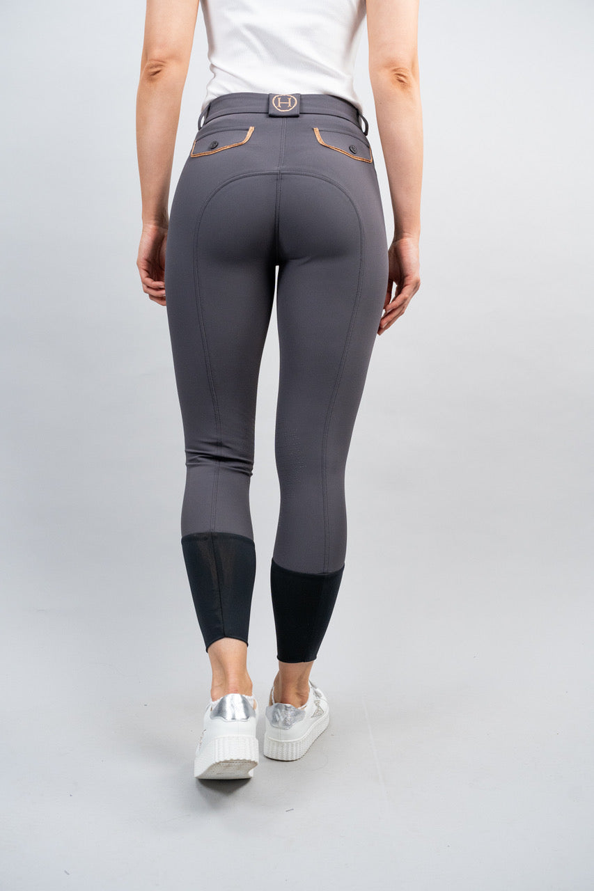 Person wearing gray riding pants with black ankle cuff on a light gray background