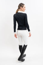 Woman wearing a black equestrian competition shirt with and white breeches on a white background