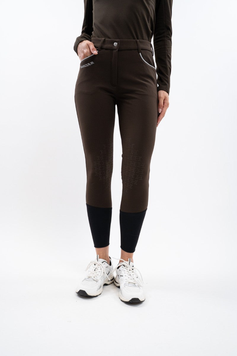 Person wearing brown riding pants with black leggings and white sneakers on a white background
