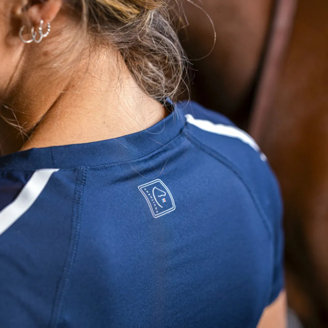Person wearing a blue shirt with a logo, standing next to a horse.