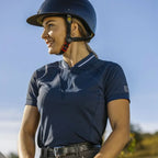Woman wearing a navy equestrian shirt and helmet against a clear blue sky.