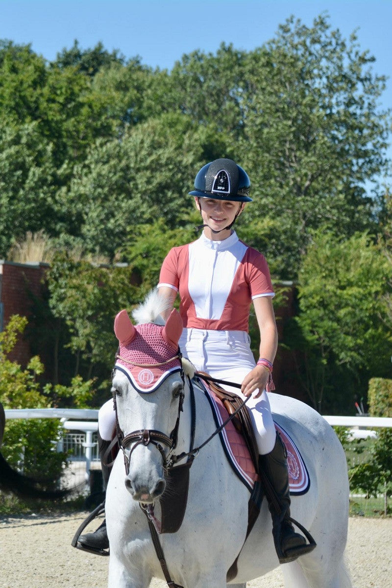 Person riding a white horse in equestrian attire with trees in the background