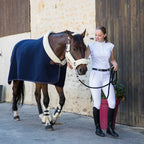 Woman in equestrian attire standing next to a horse wearing a blue rug.